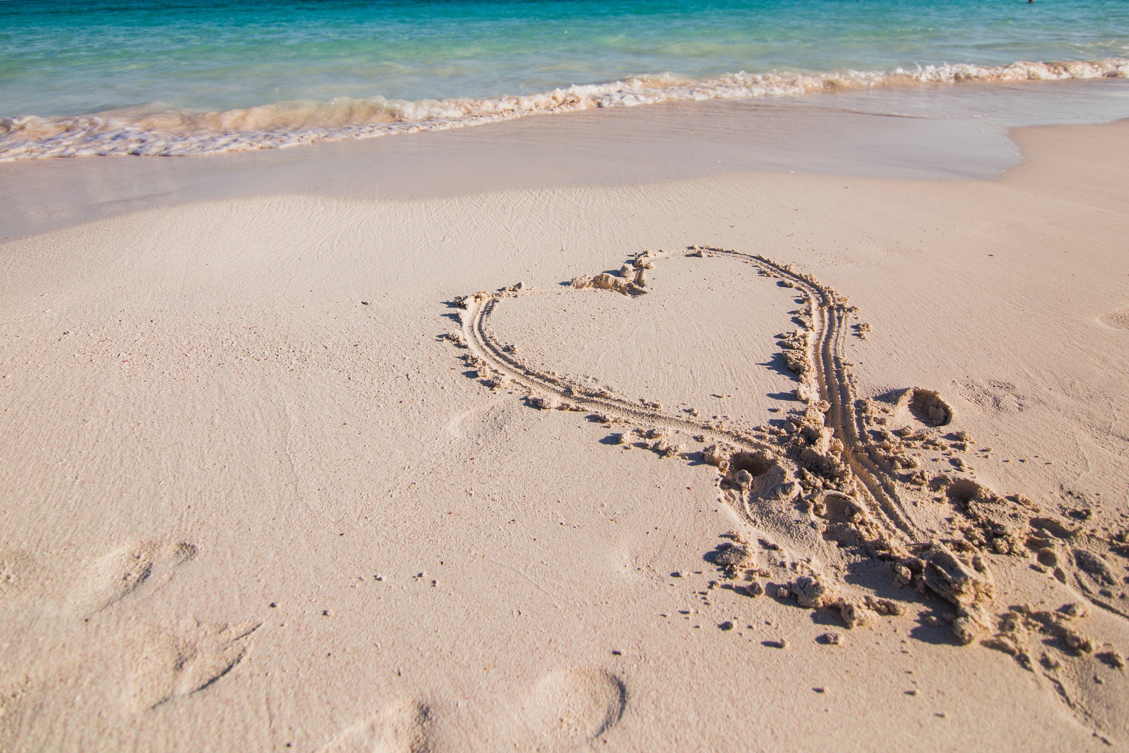 Heart drawn in the sand by ocean's side with footprints.